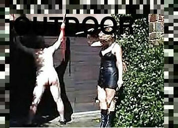 Submissive Guy With a Bondage Hood Gets Whipped By Dominatrix Outdoors