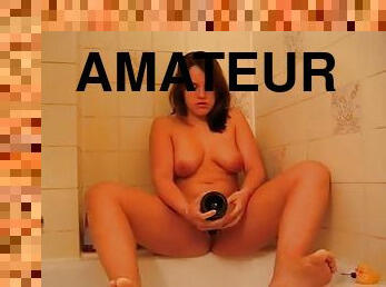 Curvy cutie sits on champagne bottle in bathtub