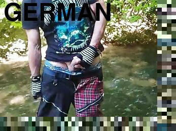 German guy stands in a creek, pisses and jerks his hard cock